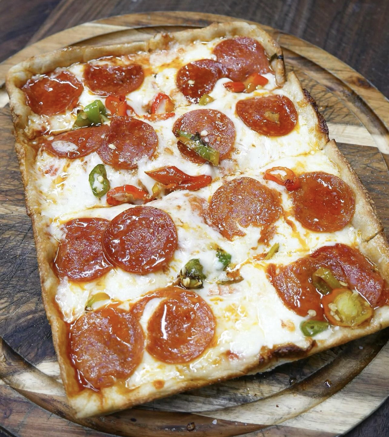 Detroit style pizza with pepperoni and hot peppers on a wooden board